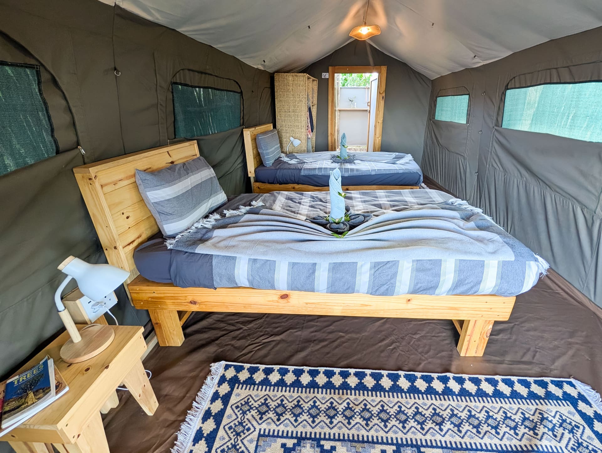 Interno di una suite tenda safari: letti in legno separati con biancheria a righe, abat-jour e tappeto a fantasia