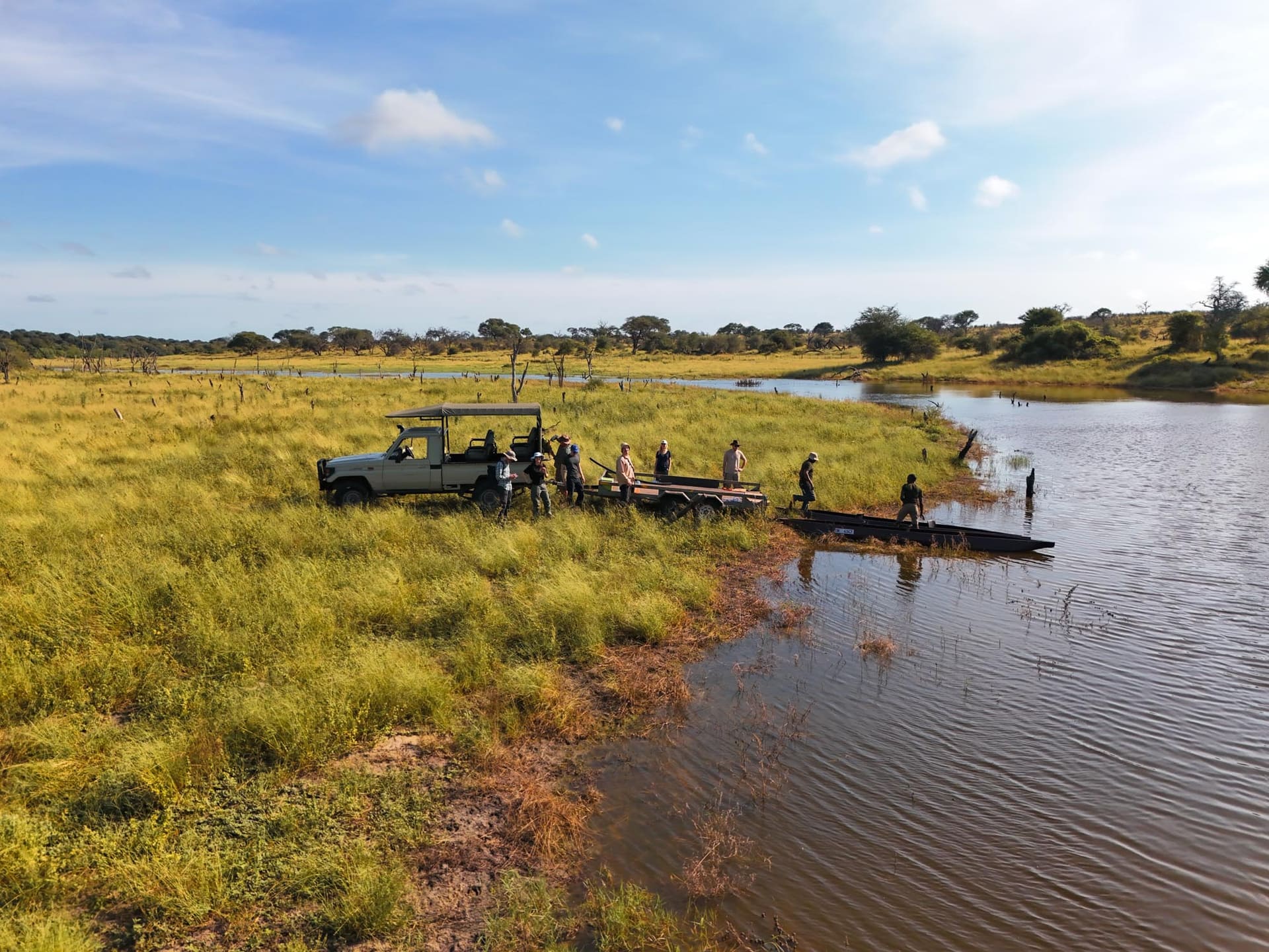 Guests beside a safari vehicle at the river